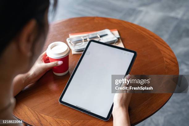 over the shoulder view of a digital tablet with a blank screen in the hands of an unrecognizable businesswoman (copy space) - holding coffee stock pictures, royalty-free photos & images