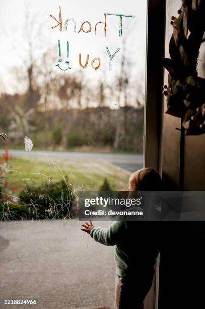 toddler at glass storm door looking out: glass has toddler scribbles and thank you message - stuck stock pictures, royalty-free photos & images