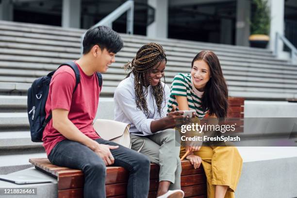 gruppe von drei universitätsstudenten, die auf ein smartphone schauen - bank student stock-fotos und bilder