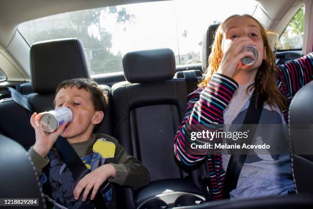 siblings sitting in the backseat of car drinking something out of a cans both drinking at the same time - drinking soda in car stock pictures, royalty-free photos & images