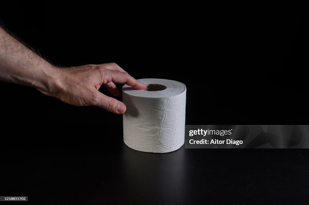 Man's hand taking a roll of hygienic paper.