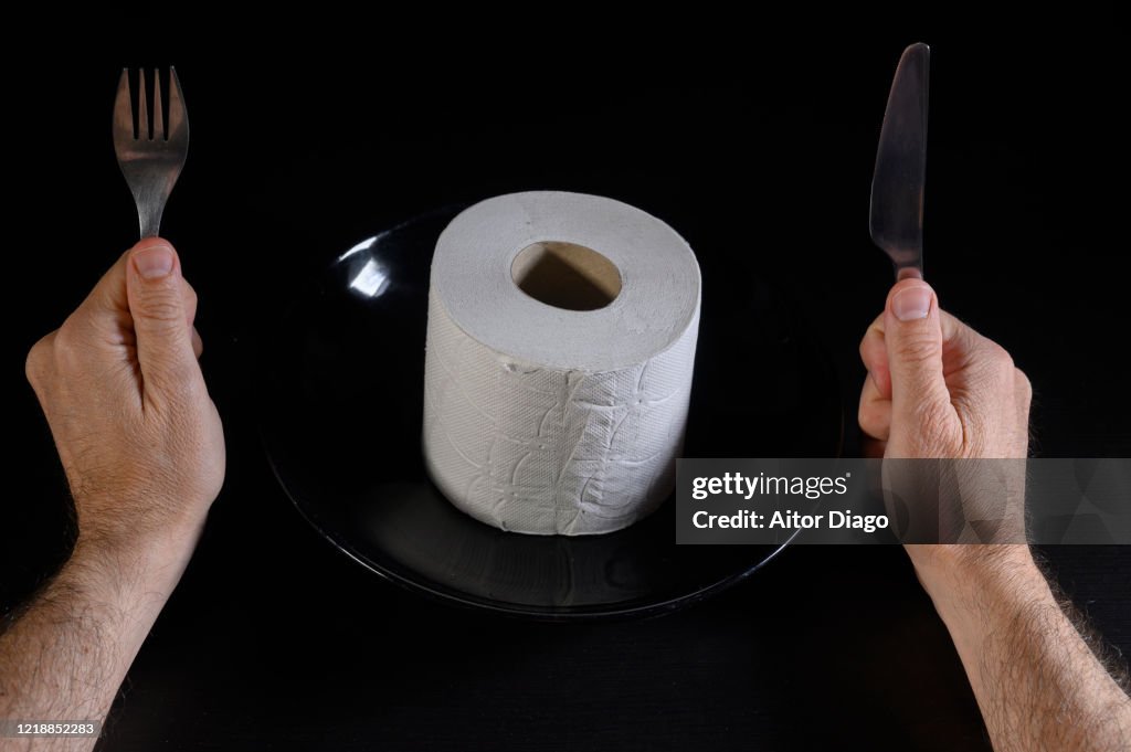 Humor. Close up of man's hands with fork and knife ready to eat a roll of toilet paper.