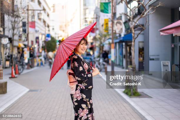 glückliche junge frau in kimono zu fuß auf einkaufsstraße - papierschirm stock-fotos und bilder