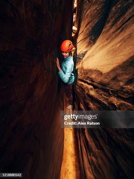 a young women squeezes her way up and through a narrow slot canyon - canyoneering stock pictures, royalty-free photos & images