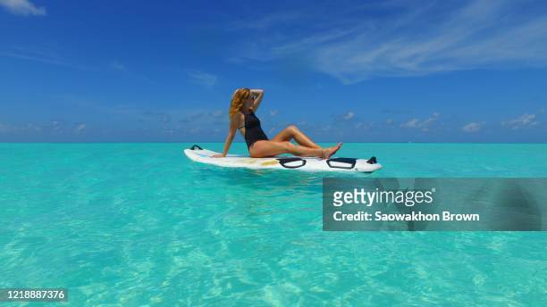 bikini girl floating on paddle board, relaxing, sunbathing. paradise, turquoise water in maldives - fashion swimwear stock pictures, royalty-free photos & images