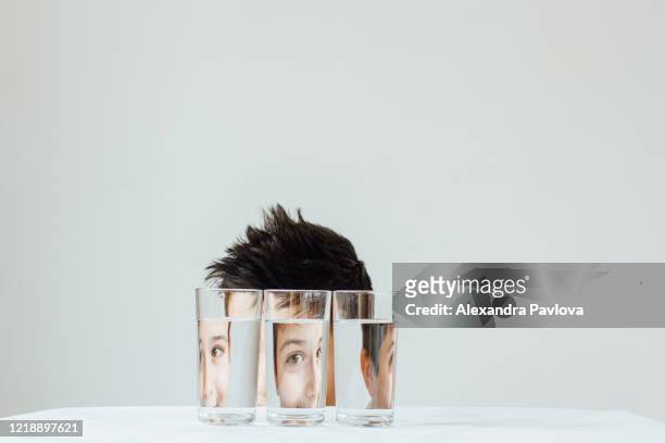 portrait of a child pulling silly face looking through water filled glasses - mirar a través fotografías e imágenes de stock