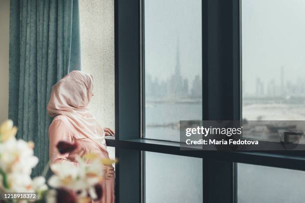 pregnant muslim woman standing near the window - lockdown loneliness stock pictures, royalty-free photos & images