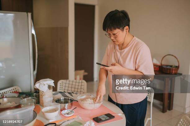an asian chinese stay home mother preparing dough while using phone online checking for for recipe and guidance online class