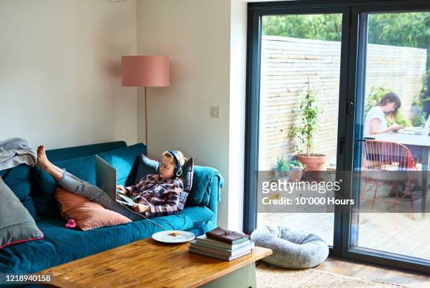 girl resting on sofa with laptop during lockdown - streaming music stock pictures, royalty-free photos & images