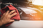 Hand is cleaning car headlight with a using red microfiber cloth.