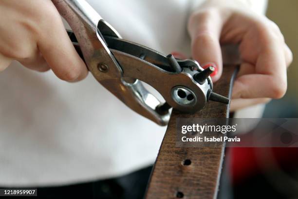 woman hands making hole with equipment on leather belt - leather belt fotografías e imágenes de stock