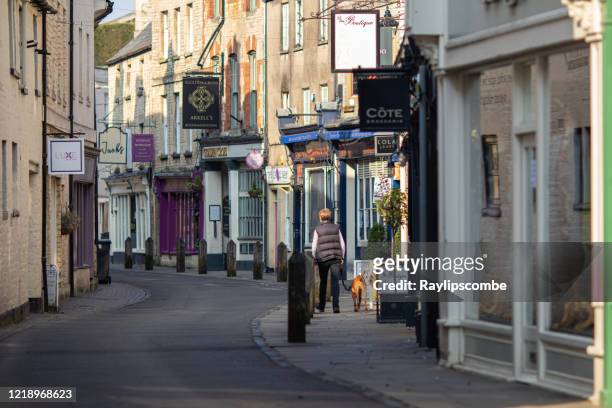 lone woman walking her dog down the deserted quaint black jack street in cirencester, gloucestershire during the coronavirus outbreak during spring 2020 - cirencester stock pictures, royalty-free photos & images