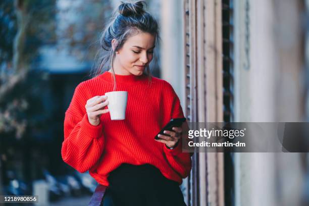 young woman drinking coffee and texting - red drink stock pictures, royalty-free photos & images