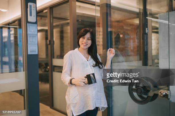 une femme enceinte chinoise asiatique frappant la porte en verre de sa salle de directeur et retenant une tasse de boisson chaude souriant - knocking photos et images de collection
