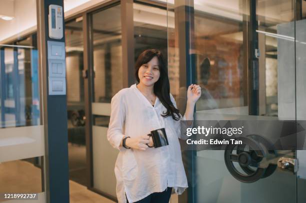 een aziatische chinese zwangere vrouw die glasdeur van haar managerruimte klopt en een kop hete drank hete glimlacht houdt - knocking stockfoto's en -beelden