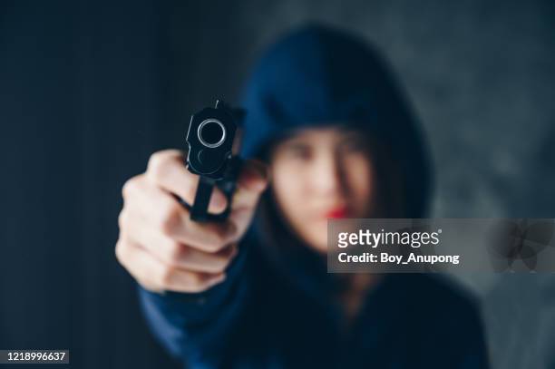 cropped shot of female criminal (or thief) wearing hood and aiming handgun to the target. - female gangster stock pictures, royalty-free photos & images