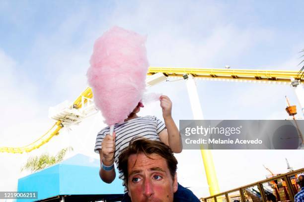a father riding his son on his shoulders with the little boy holding a big pink cotton candy in front of his face. they are in an amusement park. - cotton candy stock pictures, royalty-free photos & images