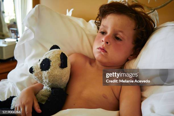 Little boy with brown curly hair laying in bed holding a stuffed panda toy.