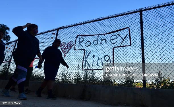 People walk past the name Rodney King seen on a chain-link fence surrounding Silver Lake Reservoir in Los Angeles, on June 9 where a new art...