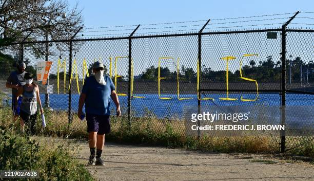 People walk past the name Manuel Ellis, seen on a chain-link fence surrounding Silver Lake Reservoir in Los Angeles, on June 9 where a new art...