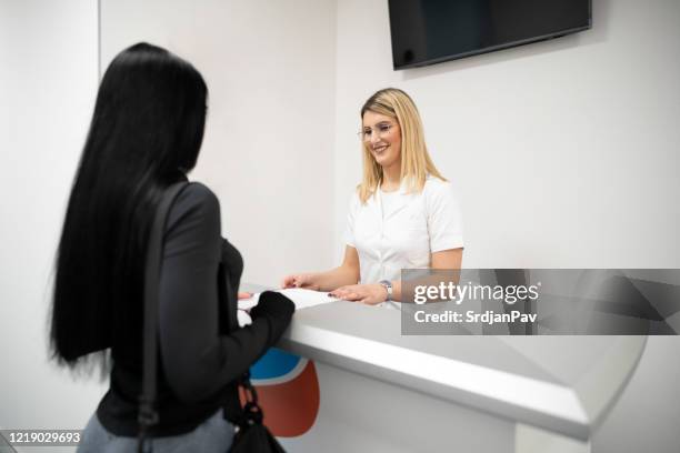 junge patientin erhält alle informationen von der krankenschwester am krankenhausschalter - arztpraxis empfang stock-fotos und bilder