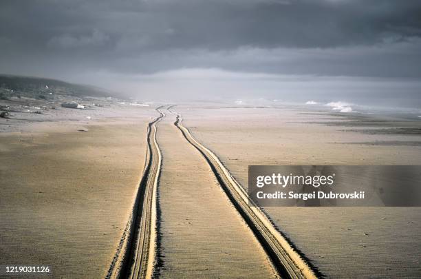 trail of two wheels of car drove along the wide beach - beach trail stock pictures, royalty-free photos & images