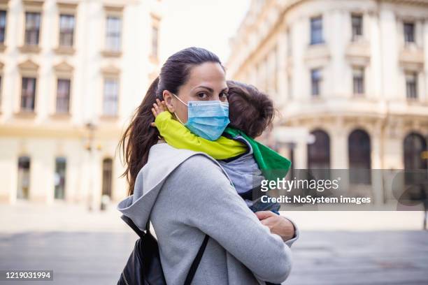mother holding her baby boy wearing protective mask - empty street stock pictures, royalty-free photos & images