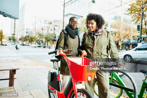 women using smart phone to rent bike share bike - mobilität zukunft stock-fotos und bilder