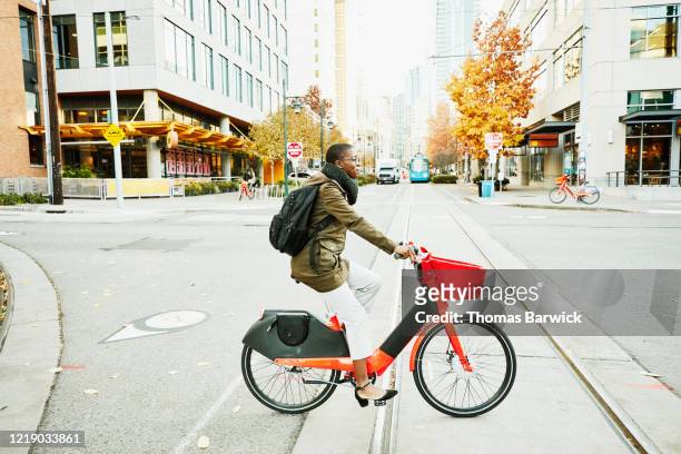 woman commuting to work on electric bike share bike - greenside stock-fotos und bilder
