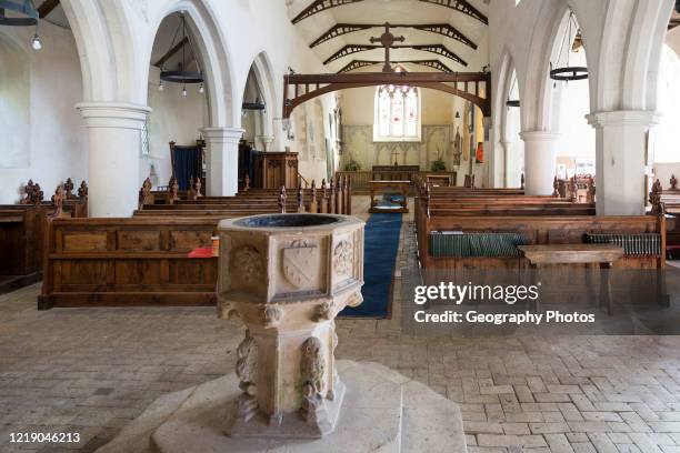 Village parish church baptismal font, Saint Nicholas, Hintlesham, Suffolk, England, UK view down wooden pews in nave to chancel and altar.