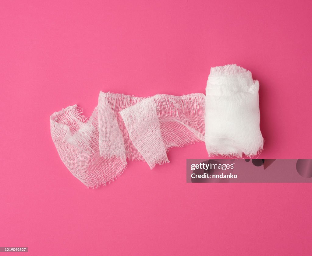 Roll of white gauze bandage on a pink background