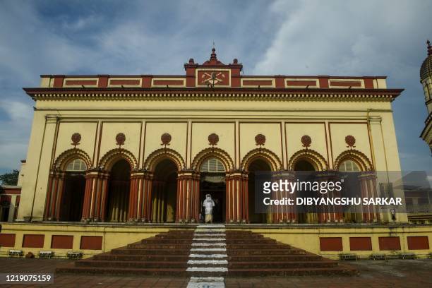 Hindu priest wearing protective gear stands waiting at the entrance stairs of the premises of the Dakshineswar Kali Temple following the reopening of...