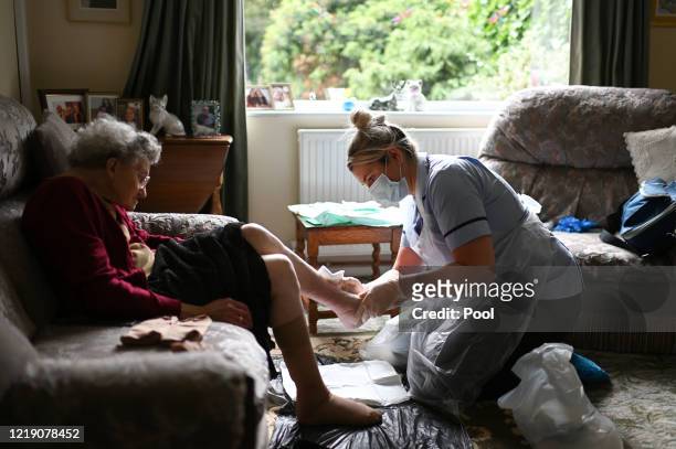 District nurse Rebecca McKenzie , wearing personal protective equipment changes the dressings on the legs of 86-year-old Margaret Ashton to treat her...