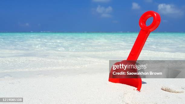 colorful beach toys and a sandy castle leftover on exotic beach with blur background of wavy sea and cloudy sky, copy space - schop stockfoto's en -beelden