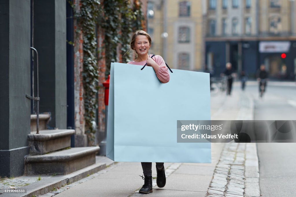 Happy girl carrying large shopping bag while walking on footpath