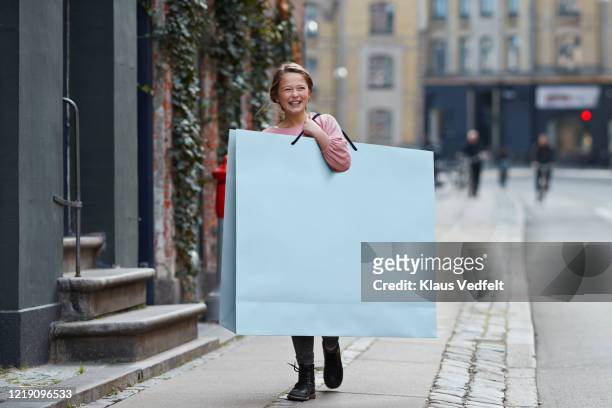 happy girl carrying large shopping bag while walking on footpath - comparison shop stock pictures, royalty-free photos & images