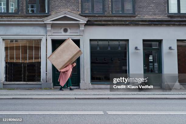 woman carrying large package on footpath in city - voll geladen stock-fotos und bilder