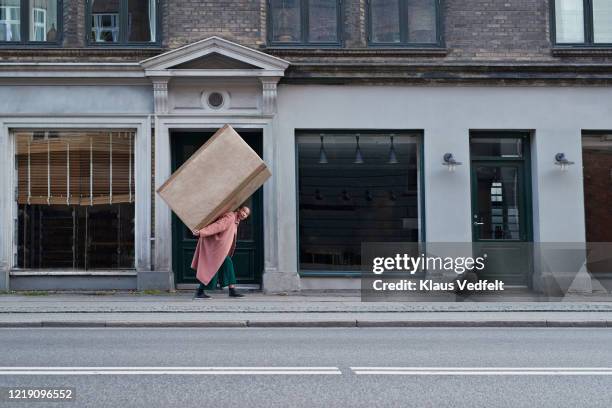 woman carrying large package on footpath in city - woman hold box imagens e fotografias de stock