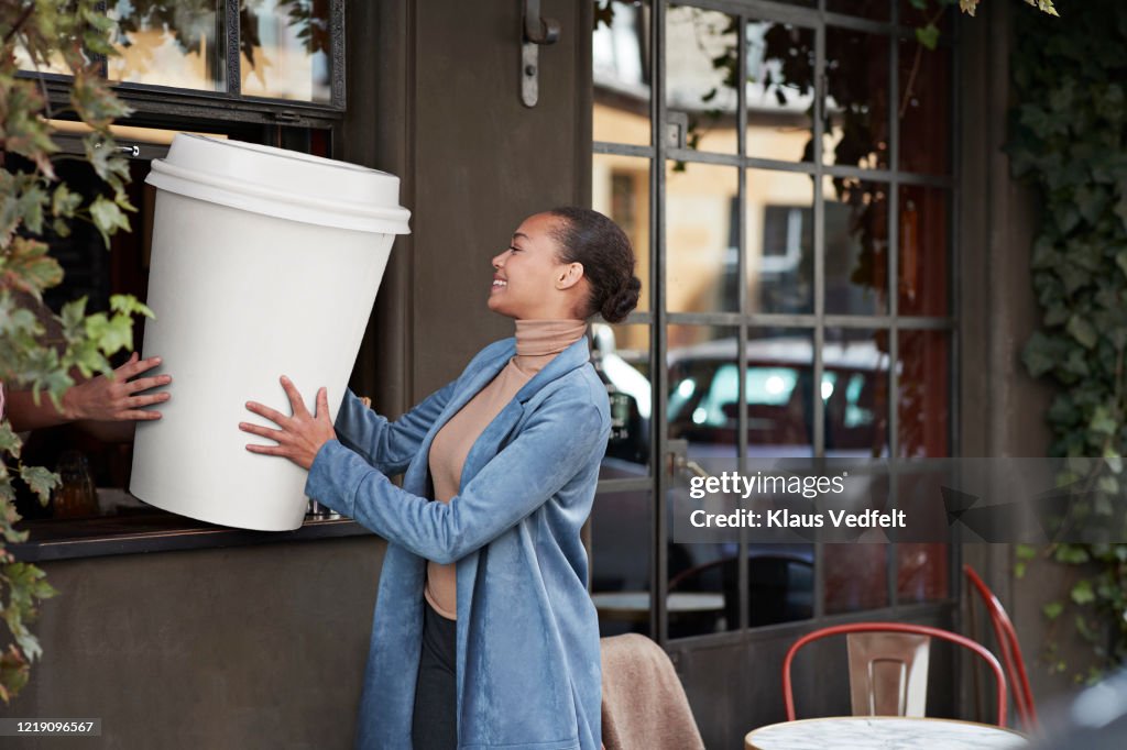 Woman holding large disposable coffee cup at take away counter of cafe