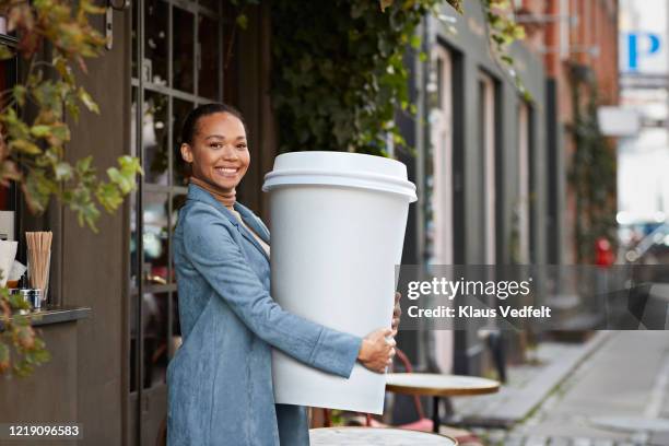 smiling woman holding large disposable coffee cup outside cafe in city - bigger photos et images de collection