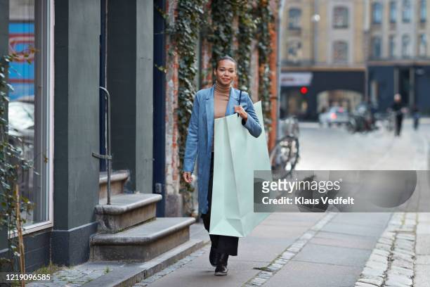 smiling woman carrying large shopping bag while walking on footpath - giant woman photos et images de collection