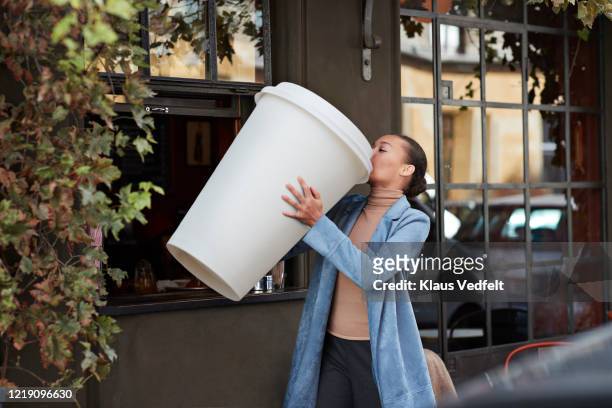 woman drinking coffee from large disposable cup at take away counter of cafe - attività del fine settimana foto e immagini stock