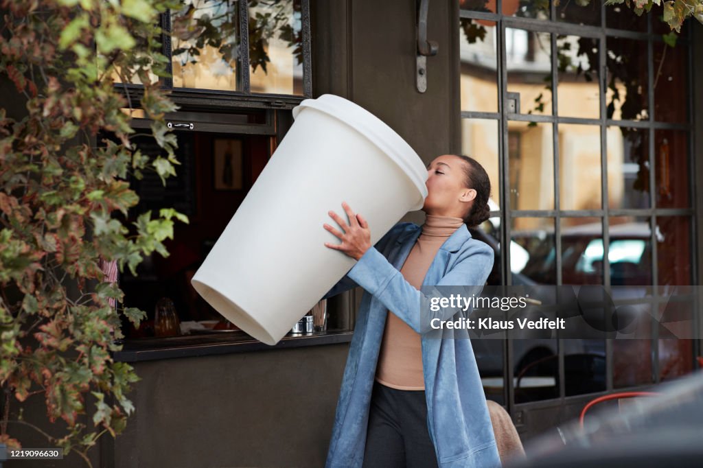 Woman drinking coffee from large disposable cup at take away counter of cafe