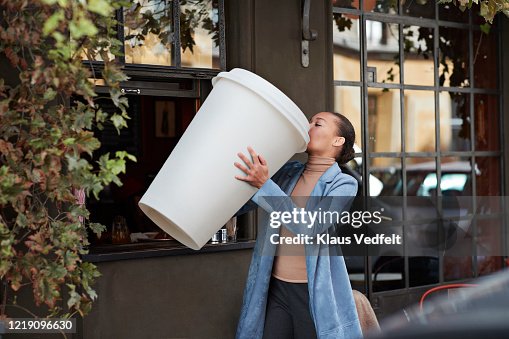 Woman drinking coffee from large disposable cup at take away counter of cafe Woman drinking coffee from large disposable cup at take away counter of cafe