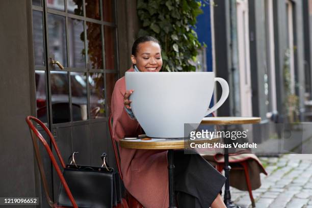 smiling woman with large coffee cup sitting at sidewalk cafe - sac à main surdimensionné photos et images de collection