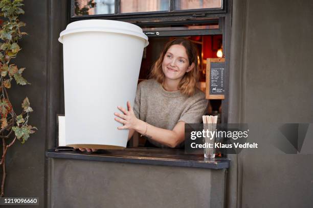 smiling barista holding disposable coffee cup at take out counter of cafe - food advertisement stock pictures, royalty-free photos & images