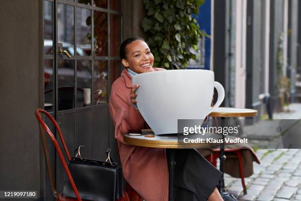 happy young woman with large coffee cup at sidewalk cafe - bolso demasiado grande fotografías e imágenes de stock