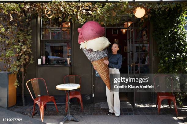 smiling woman carrying large ice cream cone at sidewalk cafe - stadt begeisterung stock-fotos und bilder