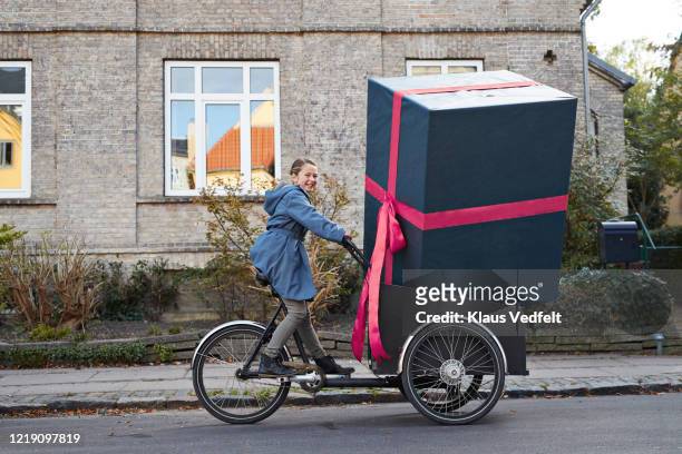 smiling girl with large gift box on bicycle cart in city - funny christmas gift stockfoto's en -beelden