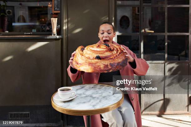 woman eating large raisin roll while sitting at sidewalk cafe - food humor stock pictures, royalty-free photos & images